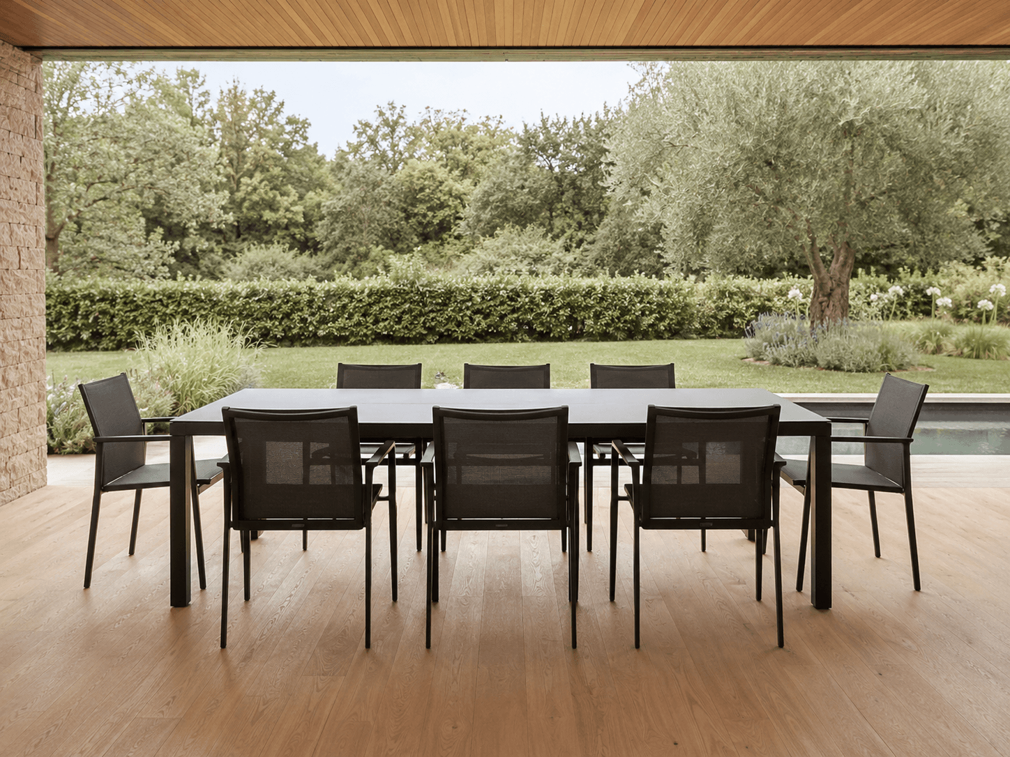 Outdoor dining table and chairs on a covered patio beside a garden